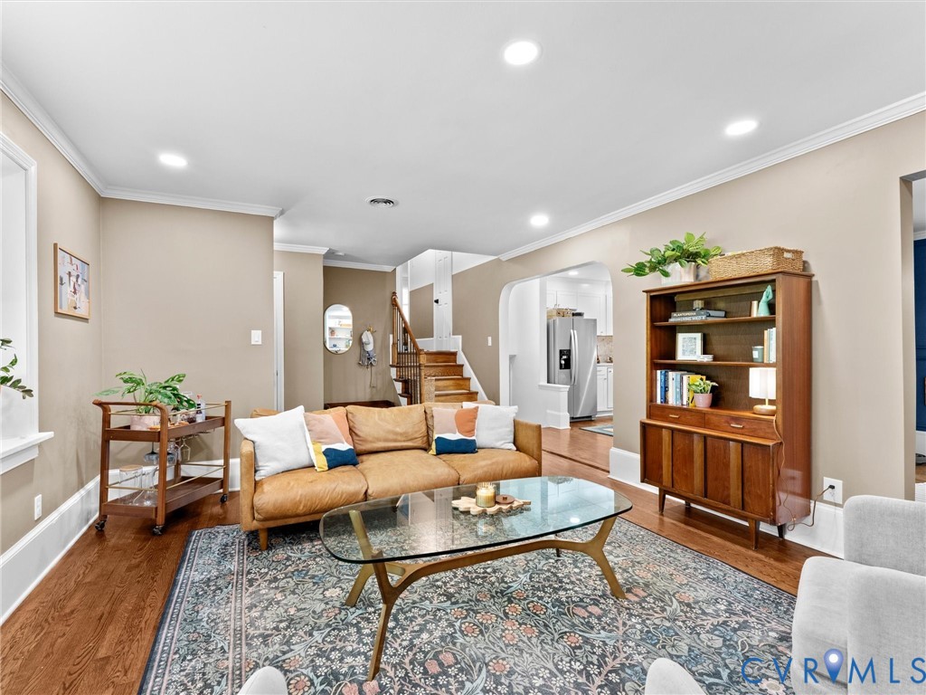 Living area featuring hardwood flooring, recessed lighting, and a neutral color palette, characterized by an arched entryway and a wooden staircase with a handrail