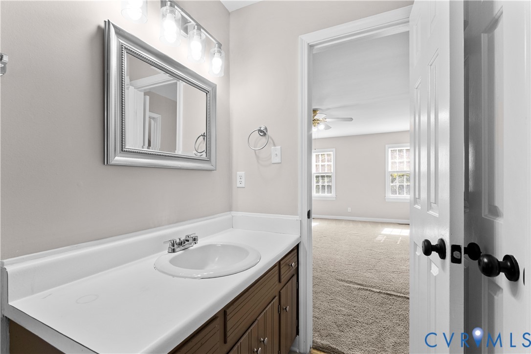 Vanity featuring a white countertop with an integrated basin, wood-finish cabinetry, framed wall-mounted mirror, and multi-bulb light fixture