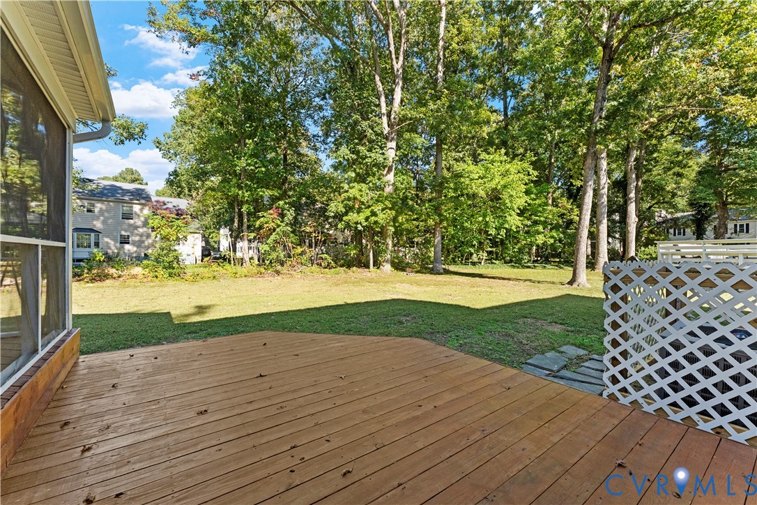Backyard featuring a wood deck, screened porch, lattice privacy panel, and mature trees