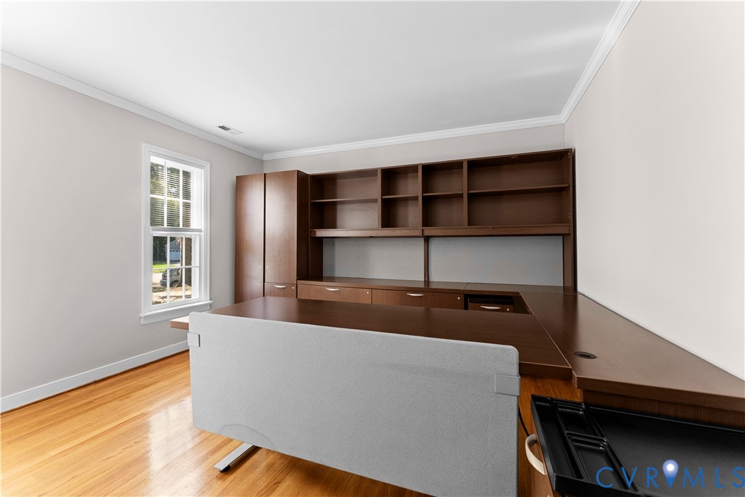 Built-in wood-finish cabinetry featuring open shelving and integrated desk surfaces, paired with wood-finish flooring and a single-hung window with white casing