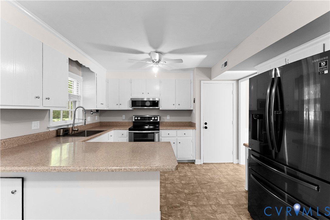 Kitchen featuring white cabinetry, solid-surface countertops, black finish appliances, built-in microwave, and a ceiling fan