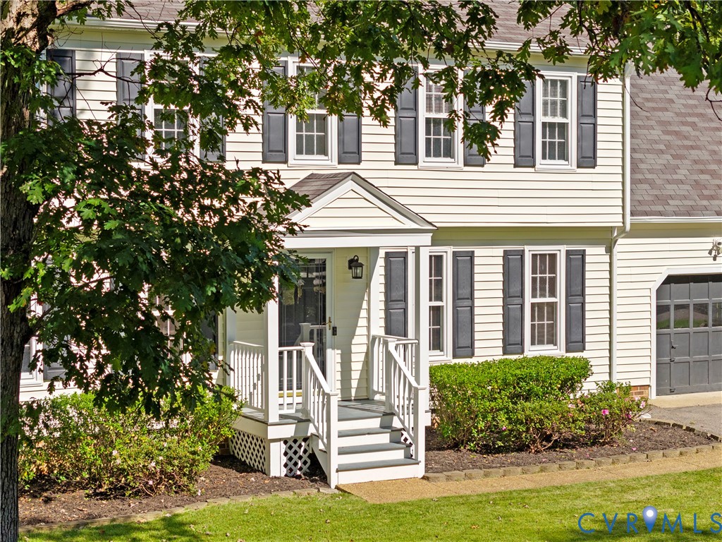 Two-story vinyl siding exterior featuring louvered shutters, a covered front porch with white railing, and an attached garage