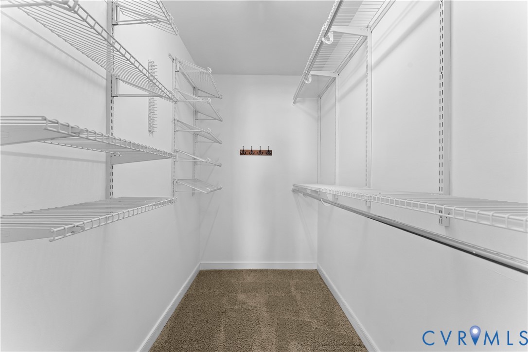 Walk-in closet featuring floor-to-ceiling white wire shelving, wall-mounted hanging rods, neutral carpeting, and an attached multi-hook rack