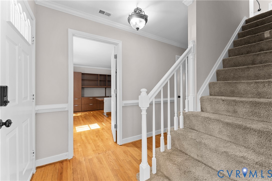 Foyer featuring wood-finish flooring, a white staircase with a wooden handrail, crown molding, chair rail trim, and a ceiling-mounted light fixture
