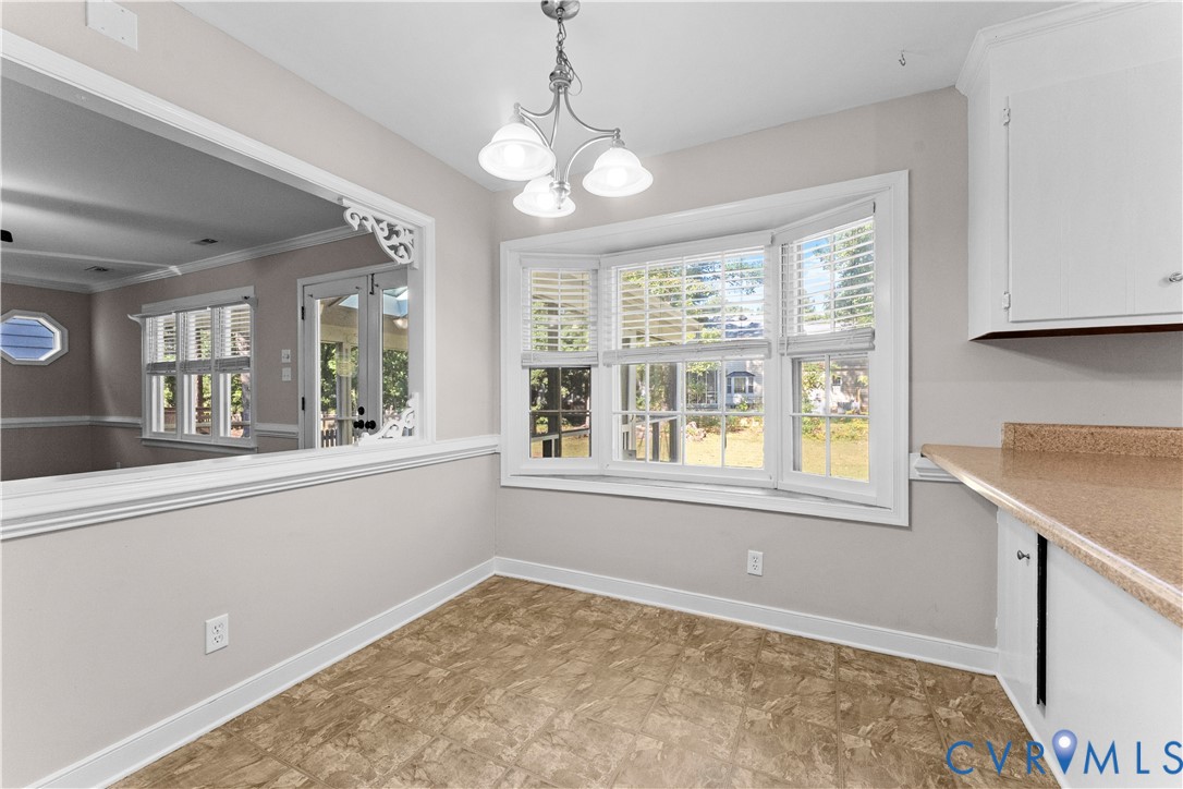 Bay window with natural light, pass-through opening with decorative corbels, three-light chandelier, and built-in cabinetry with stone-finish countertops