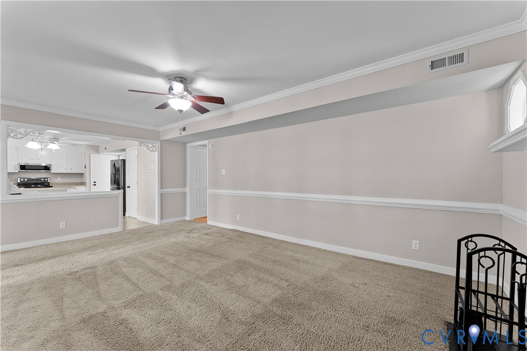 Neutral wall tones accented by chair rail molding, ceiling fan with integrated lighting, and carpeted flooring