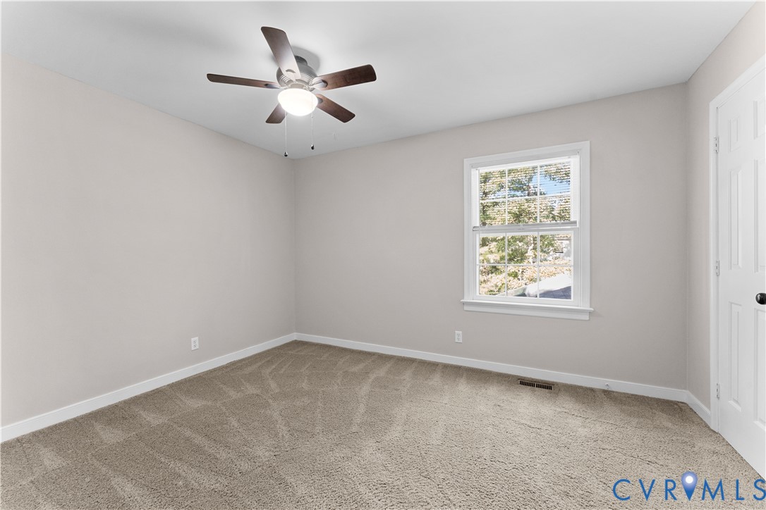 Neutral-toned interior featuring wall-to-wall carpeting, a multi-blade ceiling fan with integrated lighting, a single-hung window with muntins, and a six-panel door