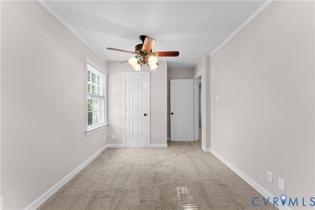 Interior space featuring neutral wall tones, wall-to-wall carpeting, a multi-pane window, and a ceiling fan with integrated lighting fixtures