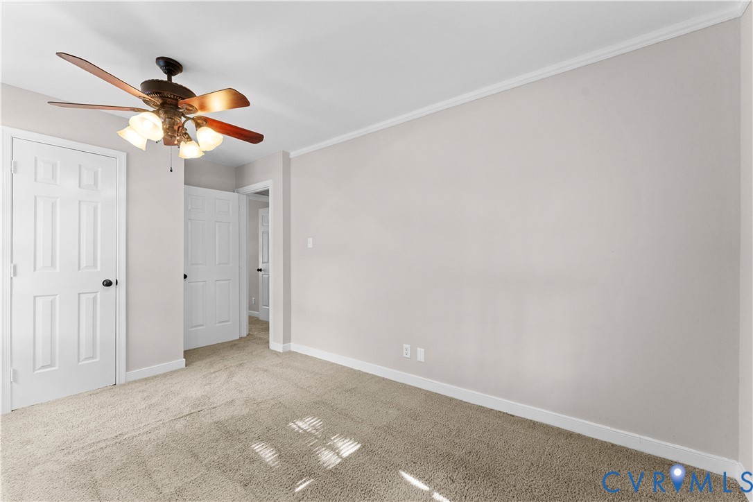 Neutral-toned interior featuring wall-to-wall carpeting, crown molding, multi-panel doors, and a ceiling fan with integrated lighting
