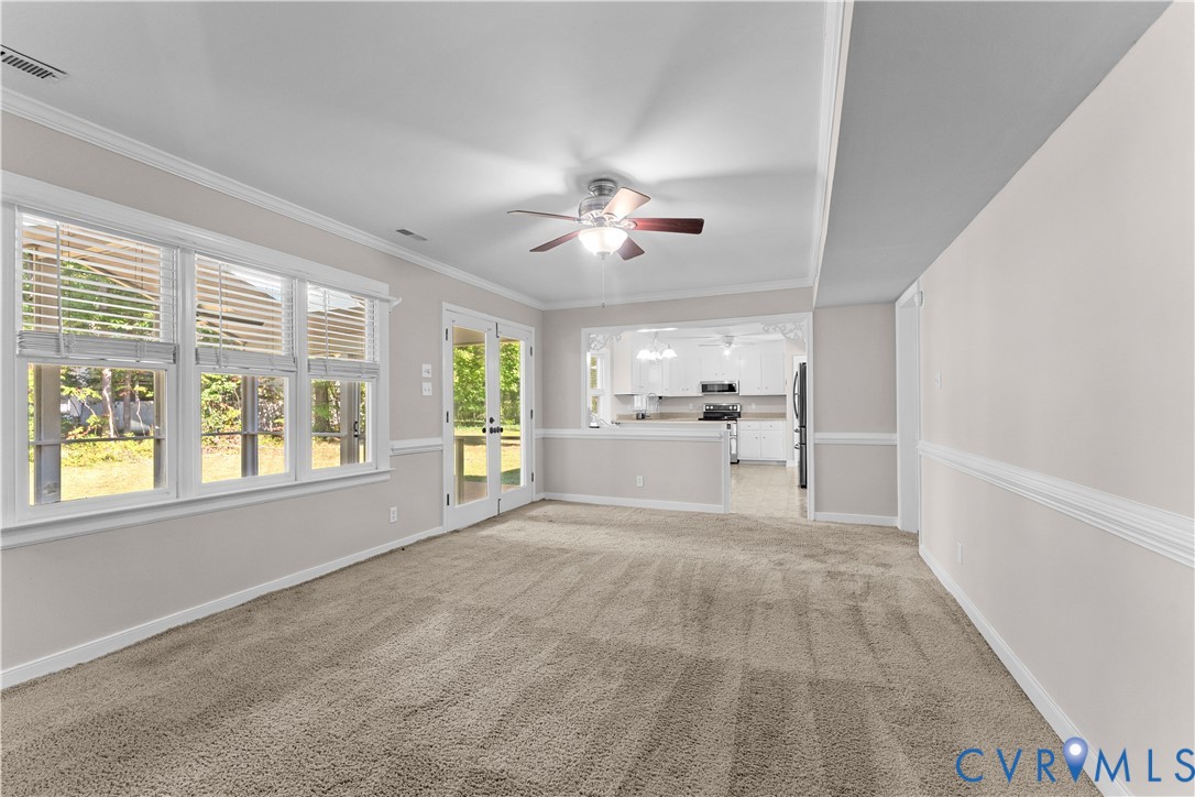 Interior space featuring neutral-toned carpeting, crown molding, chair rail trim, a multi-blade ceiling fan, and large windows with integrated blinds