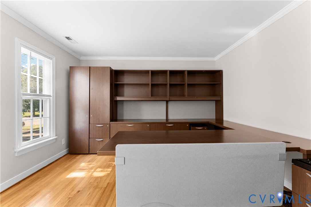 Built-in wood cabinetry with open shelving and integrated desk, wood-finish flooring, and crown molding