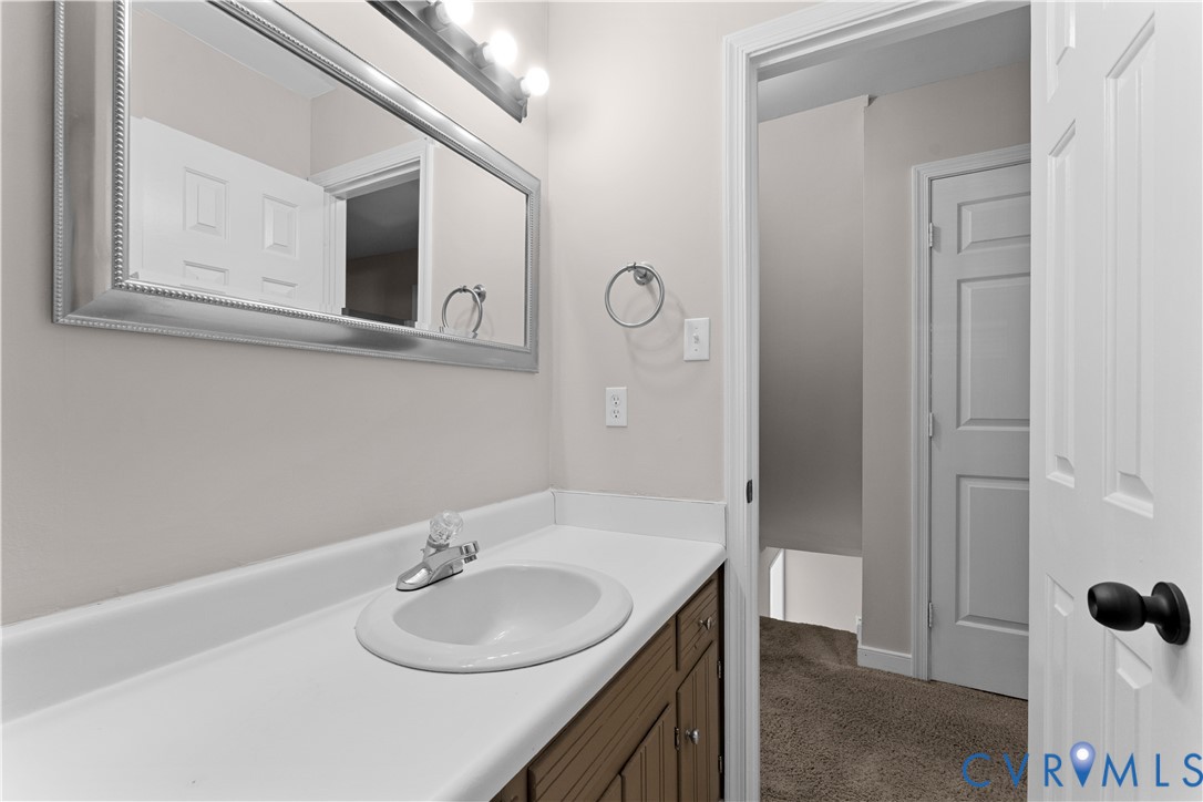Vanity featuring a solid-surface countertop with an integrated basin, wood-finish cabinetry, a large framed wall mirror, and a multi-bulb vanity light fixture