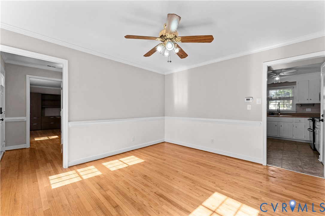 Room featuring wood-finish flooring, chair rail molding, crown molding, and a ceiling fan with integrated lighting