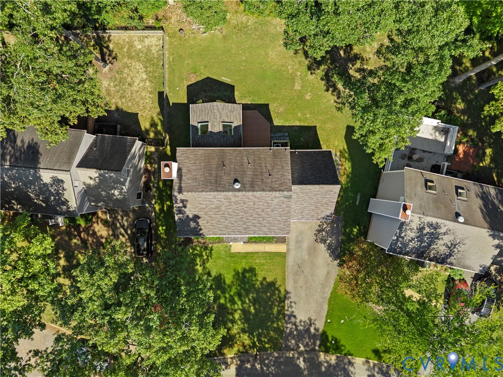 Aerial perspective of property featuring an expansive lawn, mature tree canopy, multi-pitched shingle roofing, and paved driveway