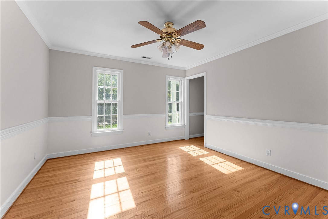 Room featuring wood-finish flooring, chair rail molding, crown molding, double-hung windows, and a central ceiling fan with integrated light fixtures