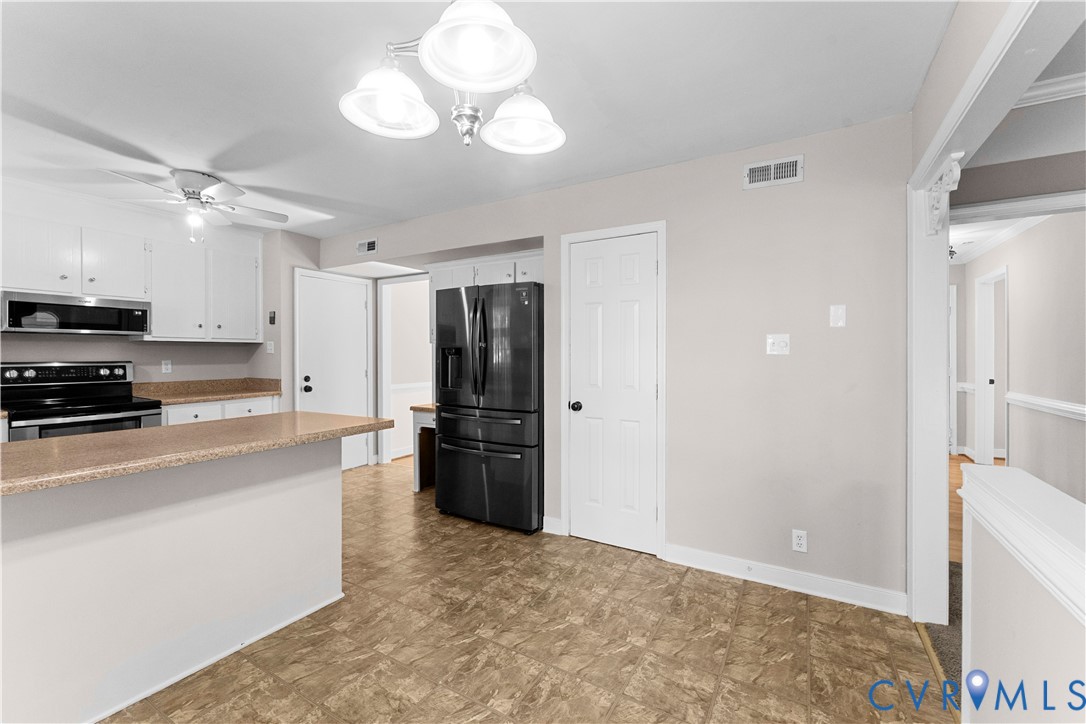 Kitchen featuring white cabinetry, solid-surface countertops, black finish appliances, and a three-light chandelier fixture