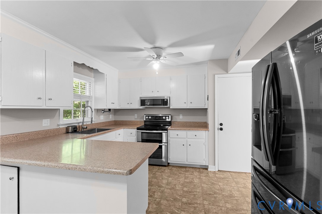 Kitchen featuring white shaker-style cabinetry, stone-finish countertops, stainless steel appliances, and a ceiling-mounted light fixture with fan
