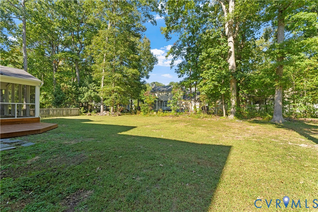 Spacious backyard featuring a grass lawn, mature trees, a wooden deck, and a screened-in enclosure