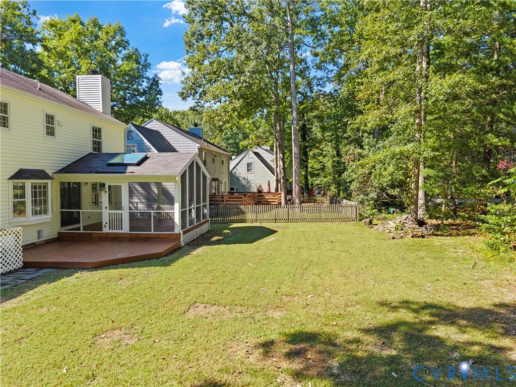 Screened porch with a skylight, wood-finish decking, and a fenced backyard featuring mature trees