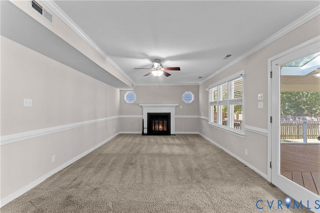 Fireplace with a white mantel, neutral wall-to-wall carpeting, crown molding, chair rail trim, and glass-paned door opening to an exterior deck