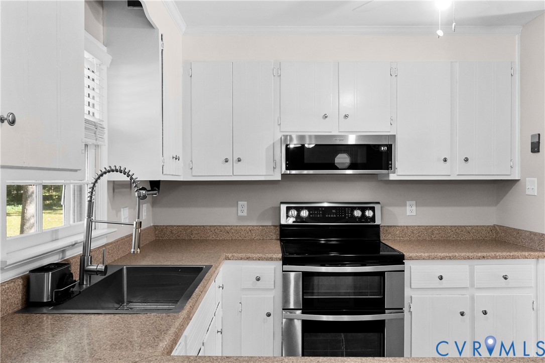 Kitchen featuring white cabinetry, solid surface countertops, stainless steel appliances, and a high-arc pull-down faucet