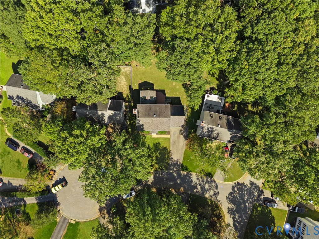 Aerial perspective featuring a residential lot with a paved driveway, mature trees, and established landscaping