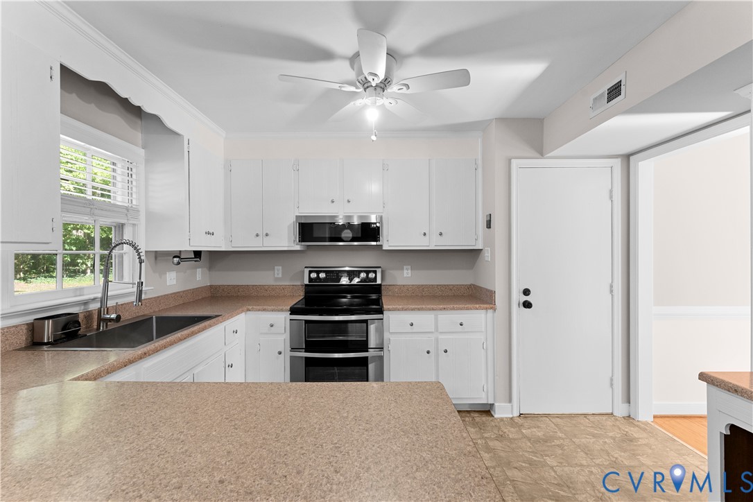 Kitchen featuring white cabinetry, solid-surface countertops, stainless steel appliances, a double-basin undermount sink with a pull-down sprayer faucet, and a ceiling fan