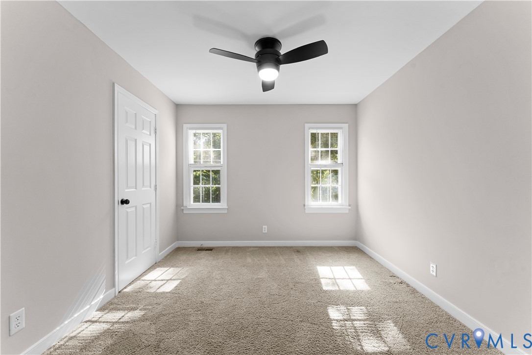 Room featuring neutral wall tones, wall-to-wall carpeting, two double-hung windows, and a matte black ceiling fan with an integrated light fixture