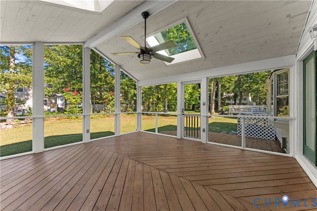 Screened-in porch featuring wood-plank decking, a vaulted wood-paneled ceiling, integrated skylights, and a ceiling fan