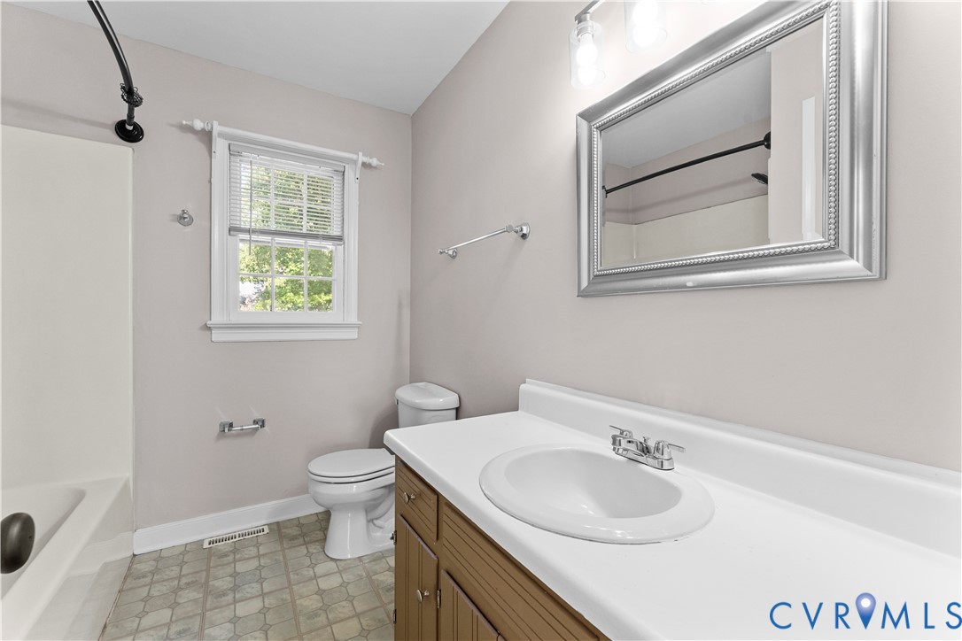 Bathroom featuring a solid-surface vanity countertop, a paneled wood-finish cabinet, a framed wall mirror, and a window with a traditional muntin design