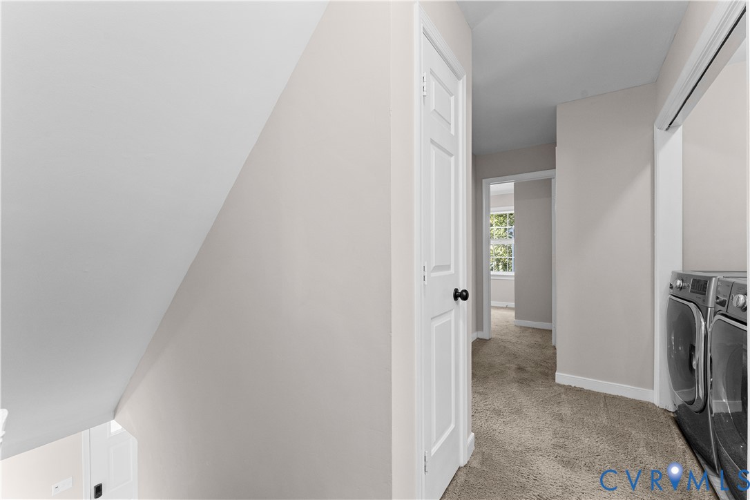 Neutral-toned interior featuring carpeting, a six-panel door with a matte black knob, and a designated laundry area with metallic-finish appliances