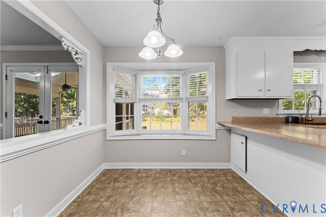 Bay window with natural light, multi-arm overhead lighting, white cabinetry, solid-surface countertop, and interior window pass-through with decorative trim