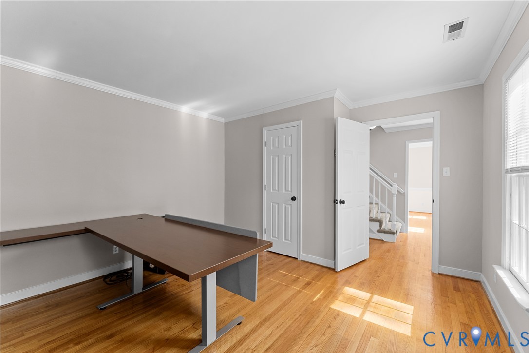 Room featuring wood-finish flooring, crown molding, and a six-panel interior door