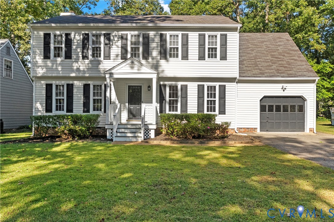 Colonial-style exterior featuring white horizontal siding, dark window shutters, an attached garage, a covered front entryway, and a landscaped lawn