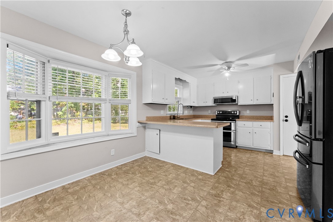 Kitchen featuring white cabinetry, a peninsula, stainless steel appliances, tiled flooring, and a triple-pane bay window