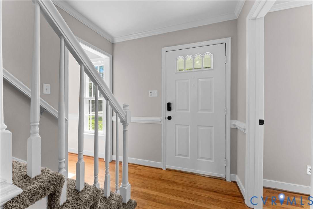 Foyer featuring wood-finish flooring, white paneled entry door with arched transom glass, staircase with white spindle balusters, and wainscoting
