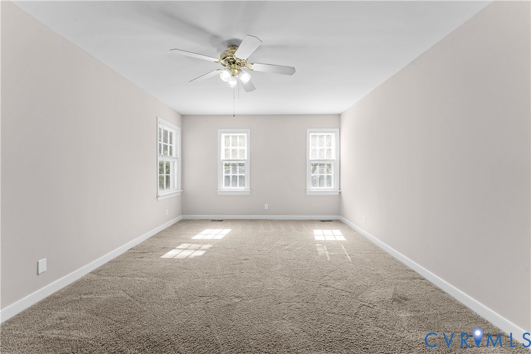 Neutral-toned interior space featuring wall-to-wall carpeting, three multi-pane windows, and a central ceiling fan with integrated lighting