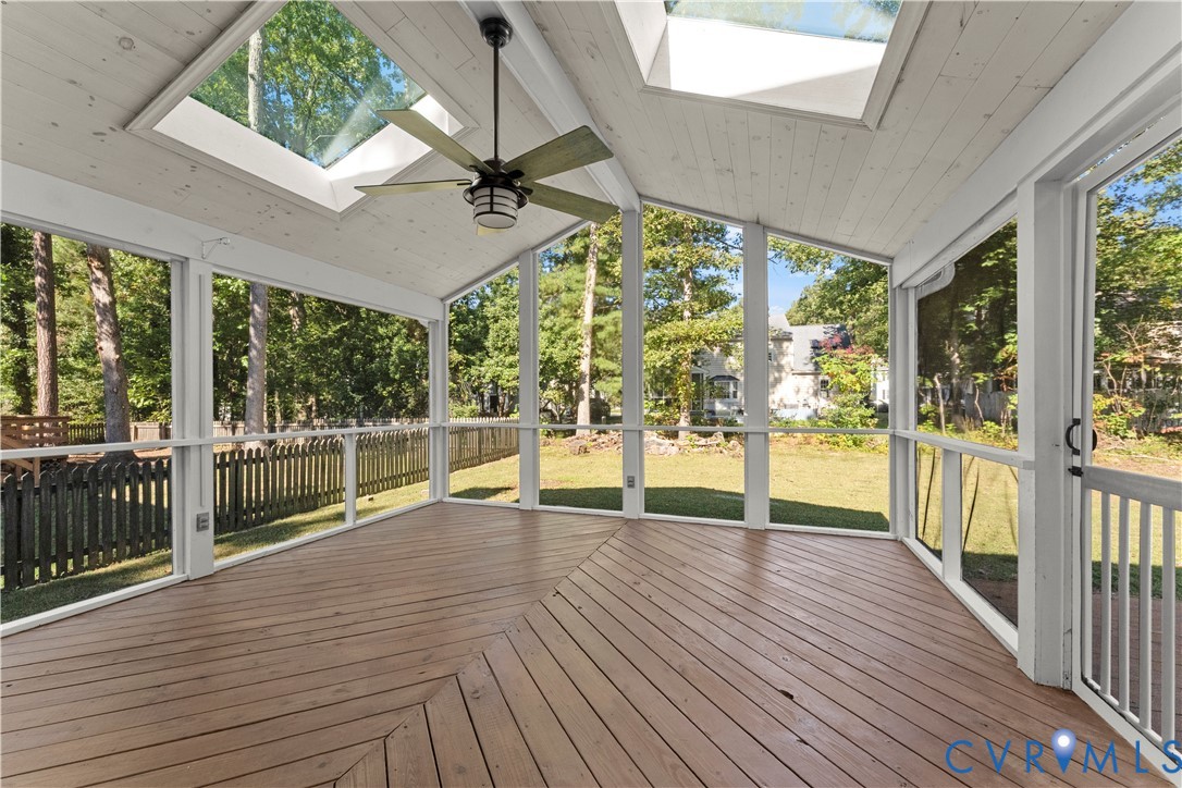 Screened-in porch featuring wood decking, vaulted ceiling with exposed beams, dual skylights, and a ceiling fan