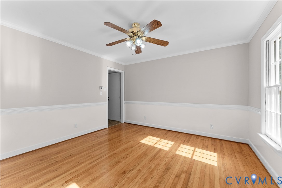 Room interior featuring wood-finish flooring, chair rail molding, multi-light ceiling fan, and multi-pane windows