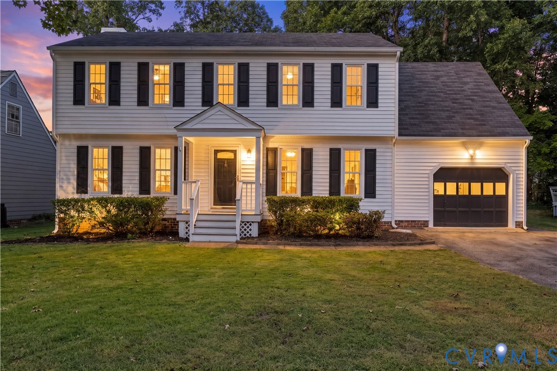 Two-story residence featuring horizontal lap siding, a covered entryway with a gabled porch, shutter-framed windows, and an attached garage with a multi-pane door Two-story residence featuring horizontal lap siding, a covered entryway with a gabled porch, shutter-framed windows, and an attached garage with a multi-pane door
