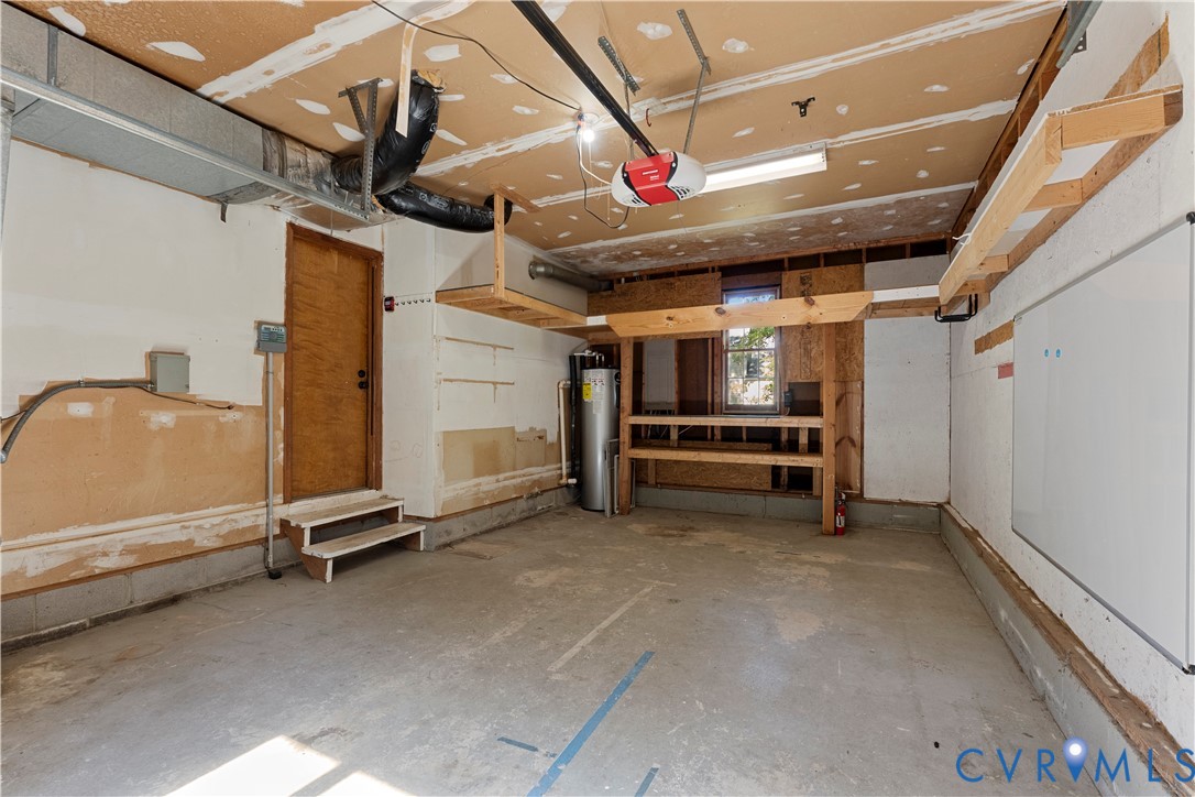 Garage featuring concrete flooring, built-in wooden shelving, a water heater, and a dedicated utility door
