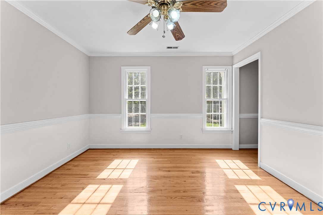 Interior space featuring wood-finish flooring, two-tone wall paint, white chair rail molding, crown molding, and a ceiling fan with integrated lighting