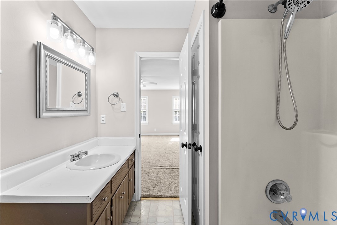 Bathroom featuring a vanity with an integrated sink and countertop, wall-mounted four-light fixture, framed mirror, and a tub-shower combination with a handheld showerhead