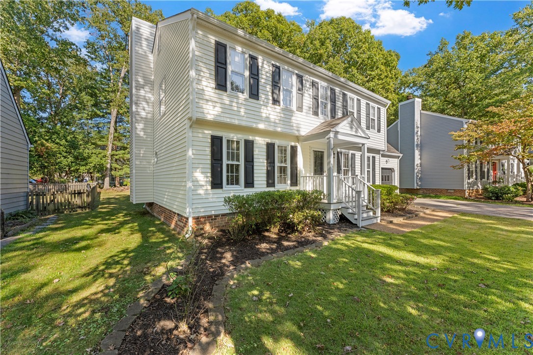 Two-story vinyl-sided exterior featuring dark shutters, a covered front entry porch, brick foundation accent, and a stone-lined garden bed