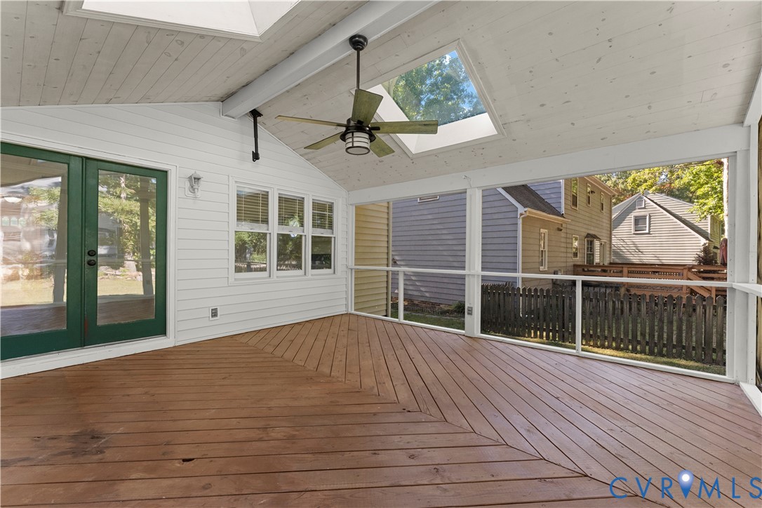 Screened-in porch featuring wood-plank decking in a herringbone pattern, vaulted tongue-and-groove ceiling, dual skylights, and a ceiling fan