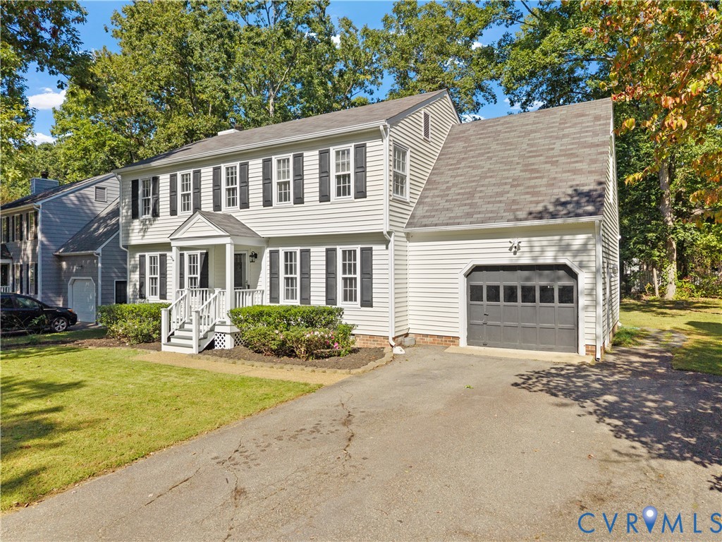 Two-story colonial exterior featuring light-colored horizontal siding, dark decorative shutters, a covered front entryway, and an attached garage