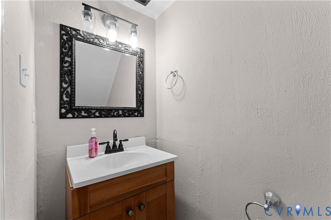 Wood-finish vanity with an integrated basin, decorative black-framed mirror, three-light fixture with clear glass shades, and matte black dual-handle faucet