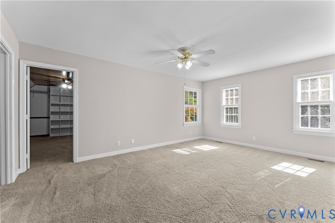 Neutral wall tones, wall-to-wall carpeting, three multi-pane windows, a central ceiling fan with integrated lighting, and built-in closet shelving