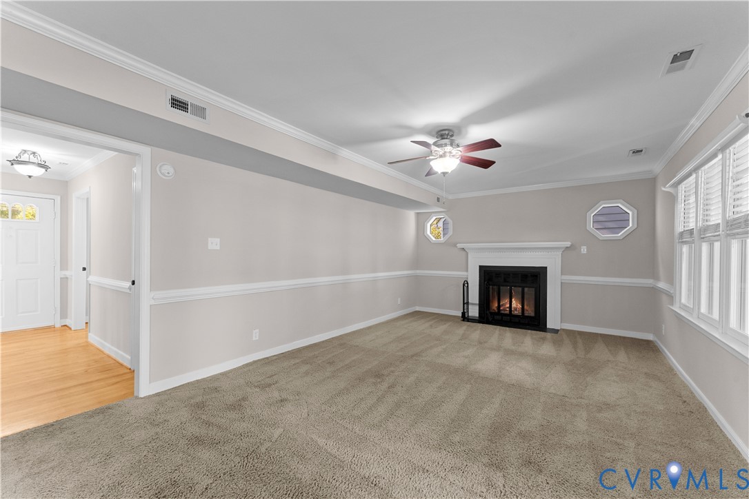 Living room featuring a fireplace with a white mantel, neutral carpeting, decorative chair rail molding, crown molding, and two octagonal accent windows