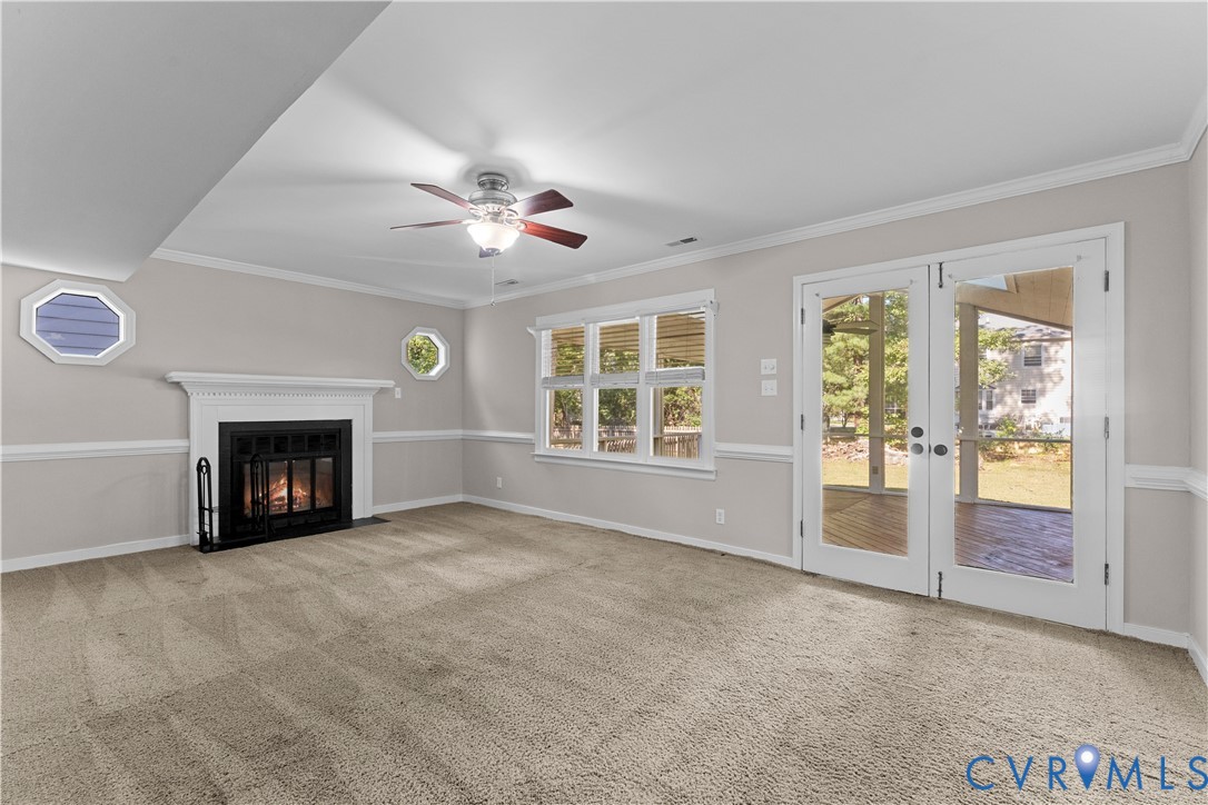 Fireplace with white mantle, multi-pane window configuration, octagonal windows, double glass-panel doors, and ceiling fan with integrated light fixture